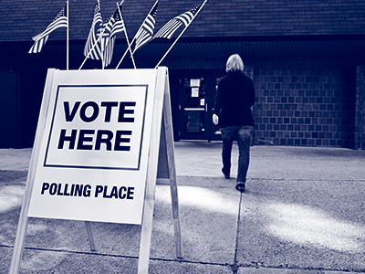 Woman walking into a building that has a sign saying "Vote here"